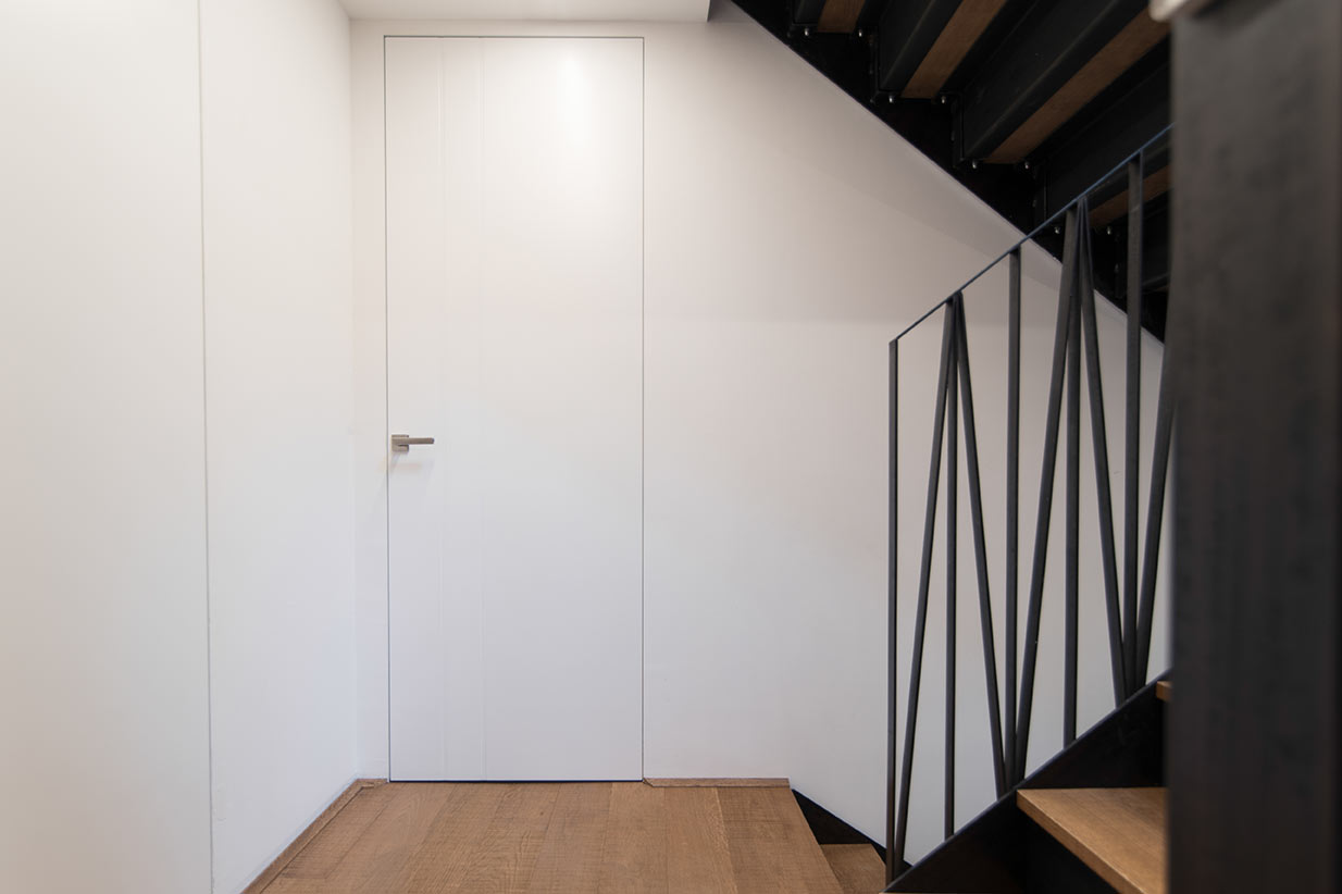 Rahmenlose weiße Tür im modernen Treppenhaus